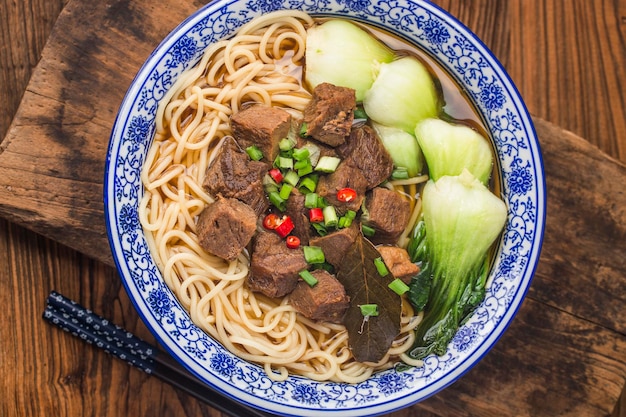 木製のテーブルのボウルにスパイシーな赤いスープ牛肉麺