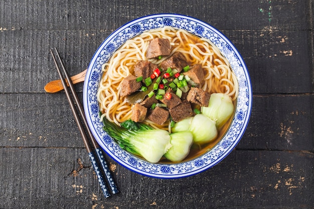 木製のテーブルのボウルにスパイシーな赤いスープ牛肉麺