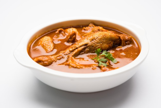 Spicy Reddish Chicken Curry or Masala, with prominent Leg Piece, served in a bowl or Kadhai over colourful or wooden background. selective focus.