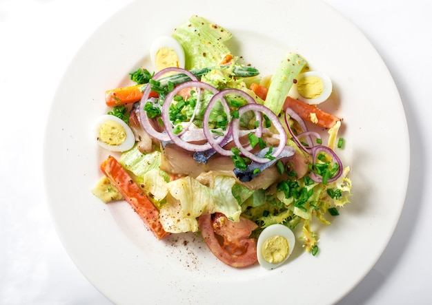 Острый салат со скумбрией, кабачками, листьями салата, морковью и сливочной заправкой с семенами горчицы в белой тарелке