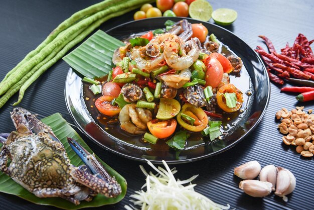 Foto insalata piccante di frutti di mare con gamberetti, granchi, coccolli serviti su piatto nero con verdure fresche, erbe e spezie menu thai food