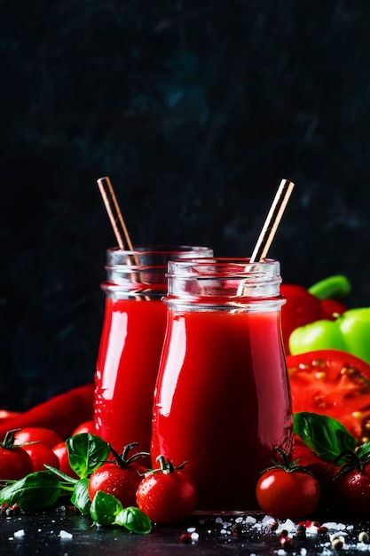 Spicy tomato juice with chili bell peppers and green basil in glass bottles on black background selective focus