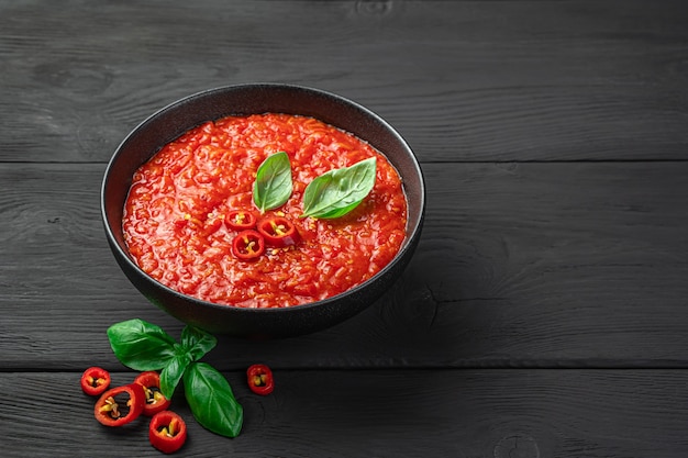 Spicy tomato sauce with basil in a bowl on a black background. Side view, copy space