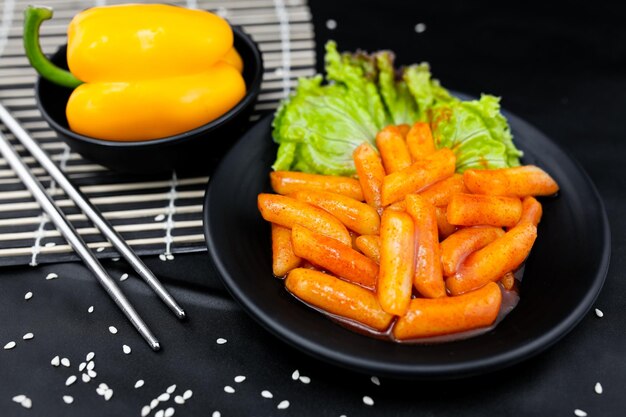 Foto tteokbokki piccante su stoviglie nere con bastoncini di metallo