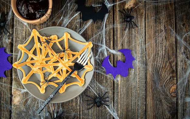 Spiders on a festive web of Halloween pancakes in a plate on a spooky wooden table Scary halloween