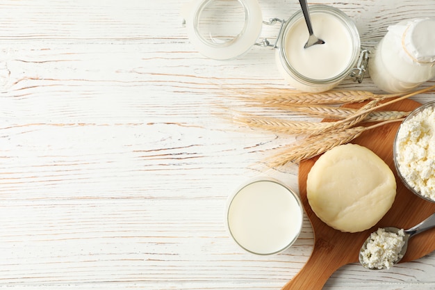 Spikelets of wheat, dairy products and board on white wood background