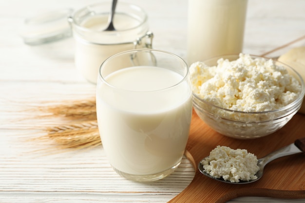 Spikelets of wheat, dairy products and board on white wood background