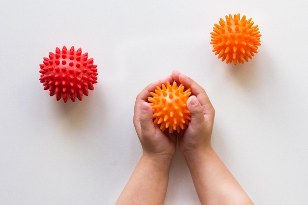 Spiky orange massage needle ball in child hands on white background