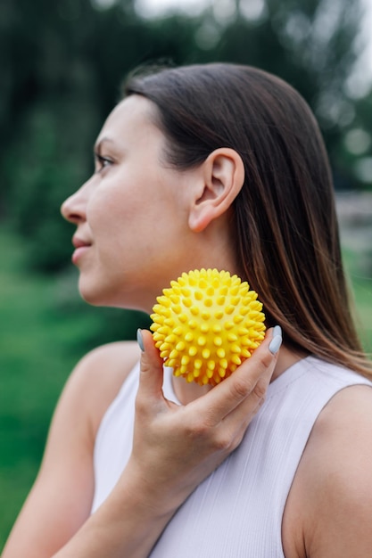 Spiky rubber massage ball for muscle recovery in hands of young woman after workout in park