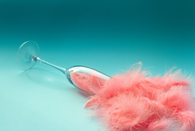 Spilled champagne glass full of pink feathers on a turquoise 