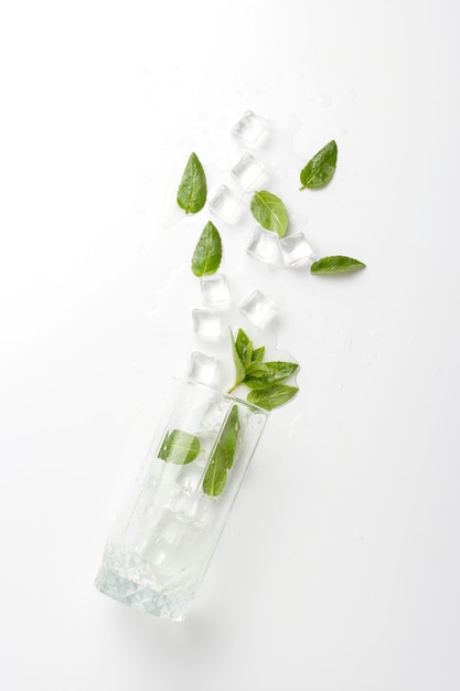 Spilled Glass with refreshing water, mint leaves and ice cubes on a light