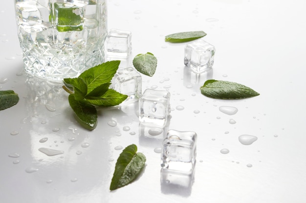 Spilled Glass with refreshing water, mint leaves and ice cubes on white surface. Flat lay, top veiw