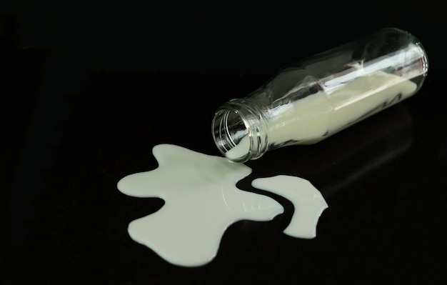 Фото Пролитое молоко из бутылки на черном фоне