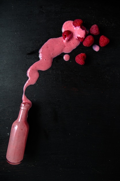 Photo spilled raspberry smoothie from bottle on black table near berry.