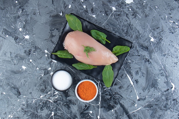 Photo spinach and chicken breast on a platter next to spice and salt bowls , on the marble surface.