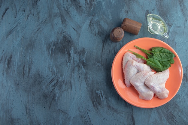 Spinaci e ala di pollo su un piatto accanto a fette di pepe e ciotola di olio, su sfondo blu.