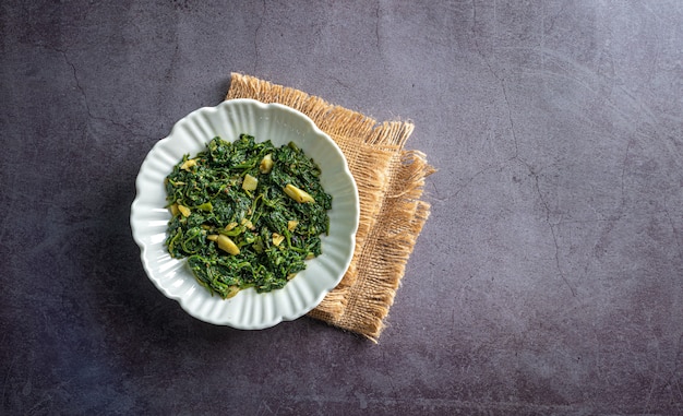 Curry di spinaci in ciotola bianca su piastrella di ardesia nera con vista dall'alto di uno strato vintage