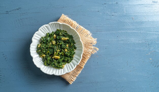 Spinach curry in white bowl on blue wooden table with a vintage layer top view