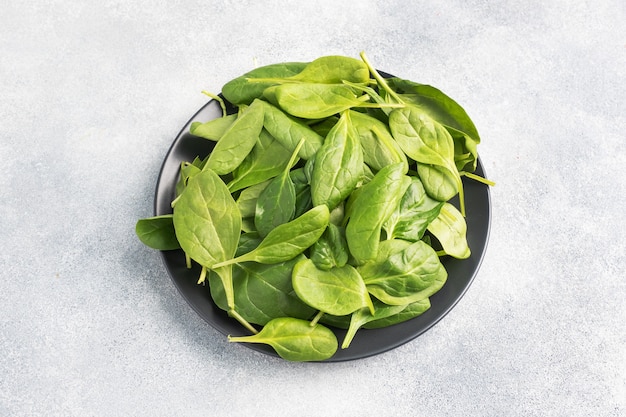 Spinach green fresh leaves on a black plate. Gray table, copy space.