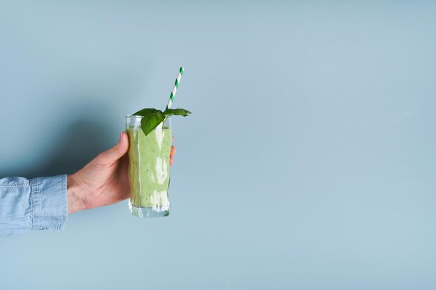 Spinach green smoothie Vegan smoothie from spinach green basil chia seeds and mint in glass in hands of female on blue background Clean eating alkaline diet weight loss food concept Mock up