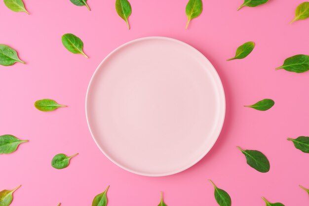 Spinach leaves around empty plate on pink background