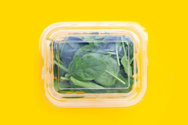 Spinach leaves in plastic box on yellow background