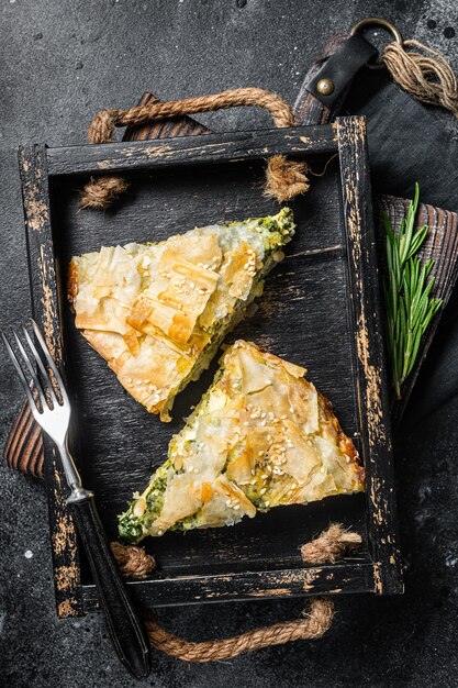 Pezzi di torta di spinaci torta greca spanakopita in vassoio di legno sfondo nero vista dall'alto