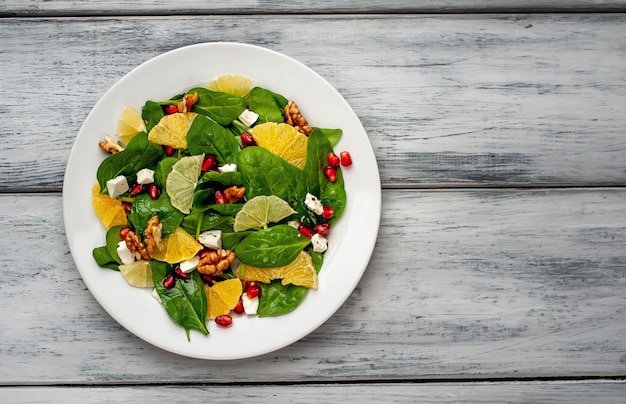 Spinach salad, orange, lemon, pomegranate, feto cheese, walnut on a white plate on a wooden table