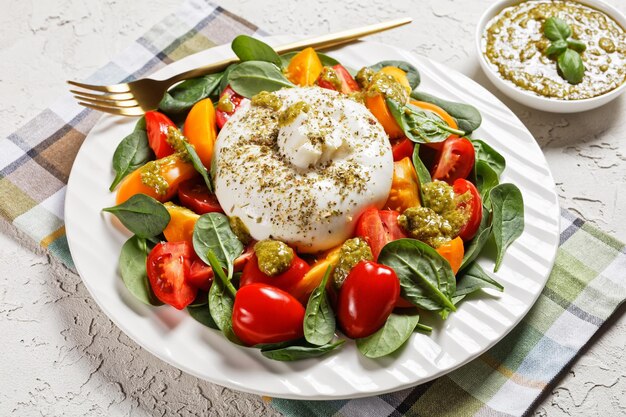 Spinach, Tomato and Burrata cheese Salad with Basil Pesto Dressing on a plate, italian cuisine