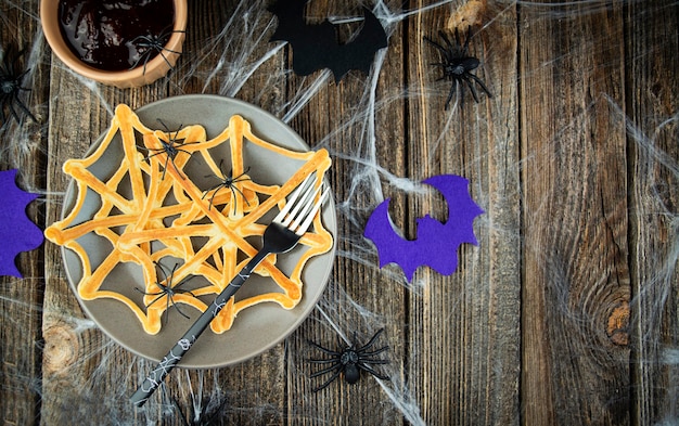 Spinnen op een feestelijk web van Halloween-pannenkoeken in een bord op een spookachtige houten tafel. Eng Halloween. Uitzicht van boven. Ruimte kopiëren