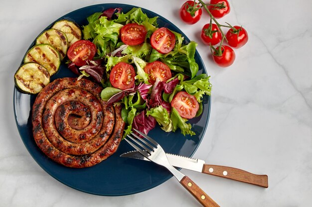 Spiral grilled sausage with tomatoes and herbs on a blue plate