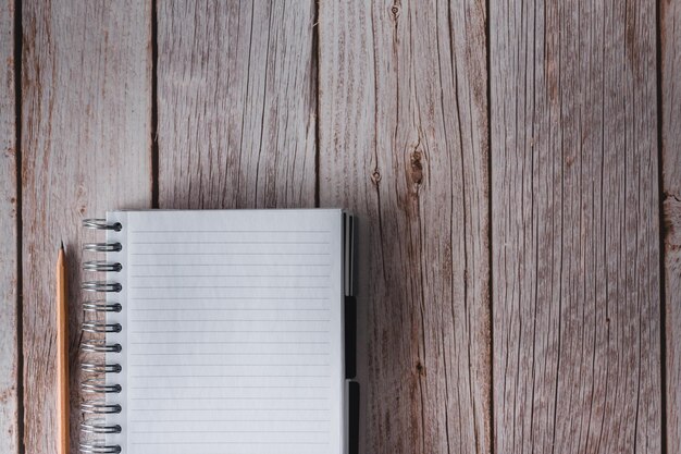 Spiral notebook in white with lines and pencil on wooden background Top view Copy space