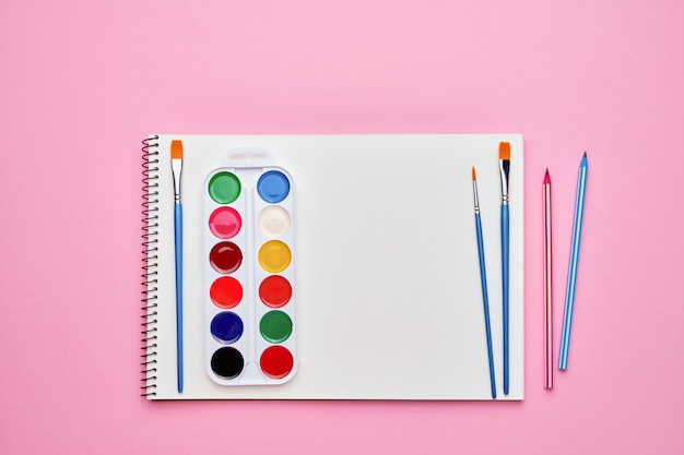 Spiral notepad with watercolors on pastel pink. Back to school concept. Copy space, top view.