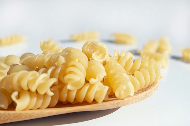 Spiral pasta lies in a wooden spoon on a white table The concept of cooking catering