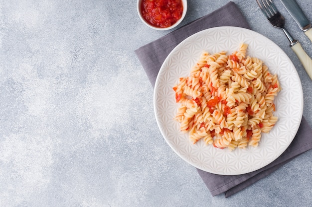 Spiral pasta mixed with cherry tomatoes and tomato sauce on a plate. Copy space