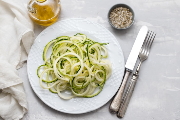 Spiral zucchini noodles on white plate on ceramic background