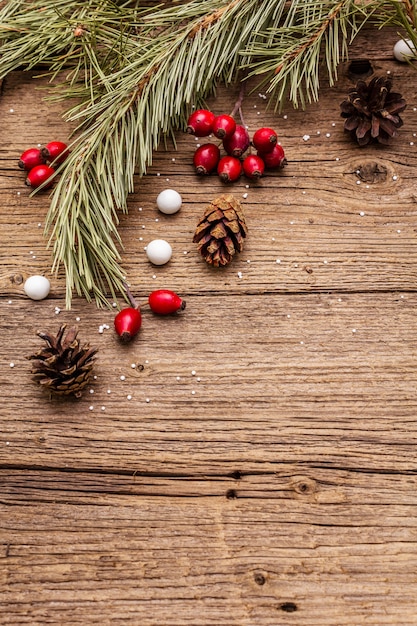 Spirit Christmas on wooden table. Fresh dog-rose berries, ball candies, pine branches and cones, artificial snow. Nature decorations, vintage wooden boards