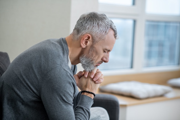 Spirituality. A gray-haired man sitting with eyes closed and saying the payers