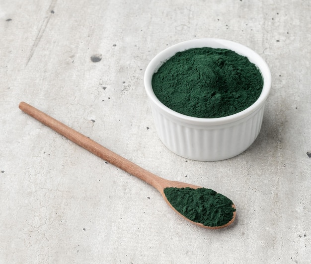 Spirulina-algenpoeder in een kom en lepel over houten tafel.