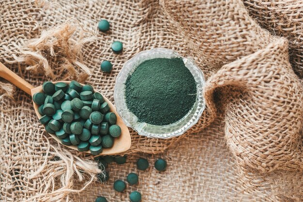 Compresse di spirulina clorella su un cucchiaio, polvere in una ciotola di vetro. super alimento per una sana alimentazione, vitamine, minerali, oligoelementi per la salute e la bellezza. superfood disintossicante.