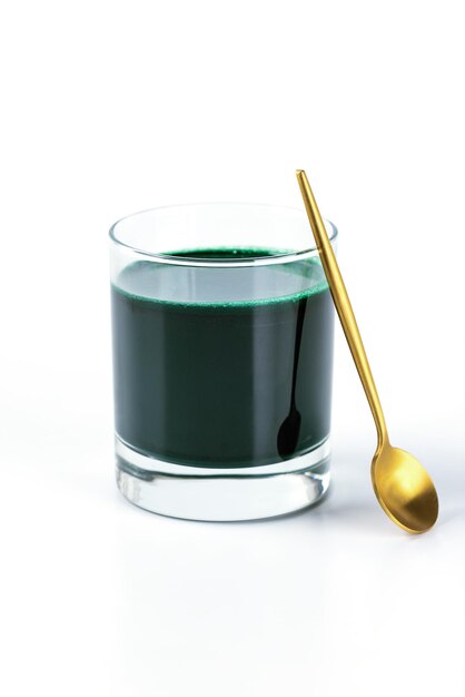 Bere spirulina in un bicchiere con un cucchiaio su sfondo bianco