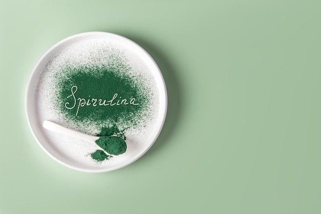 Spirulina inscription on green sprinkled spirulina powder on a white ceramic plate product presentation a copy space natural food supplements