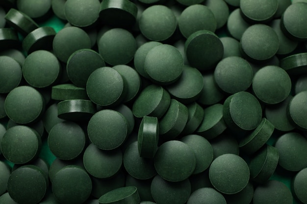 Spirulina in pills on whole background, close up