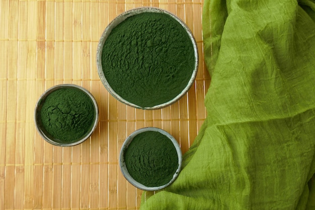 Spirulina poeder in kopjes set en groene sjaal op bamboe mat