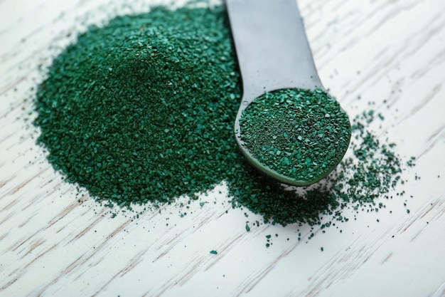 Spirulina powder and measuring spoon on wooden background