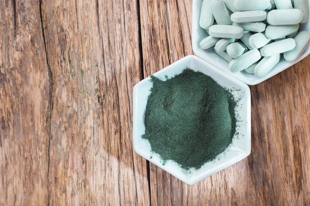 Spirulina powder and tablets on wooden background