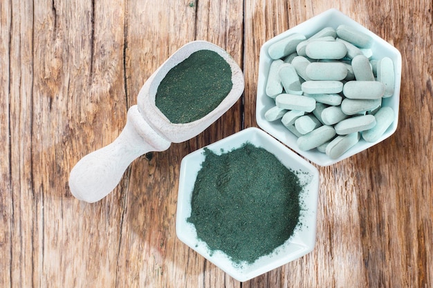 Spirulina powder and tablets on wooden background