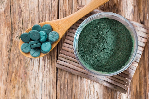 Spirulina powder and tablets on wooden background