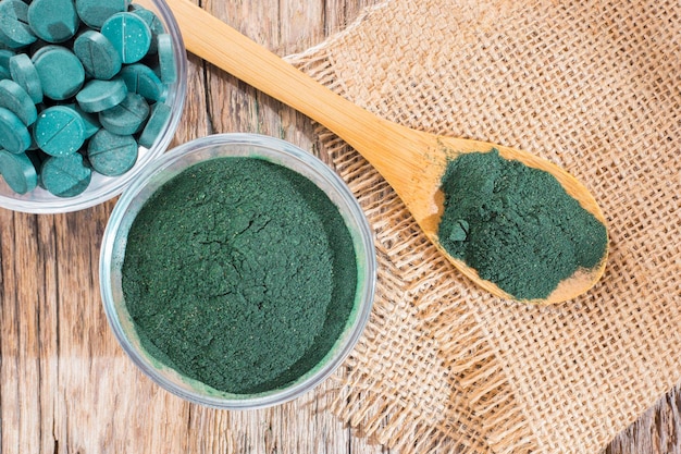 Spirulina powder and tablets on wooden background