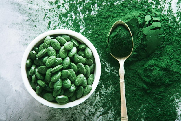 spirulina tablest in white plate and scattered powder on green background